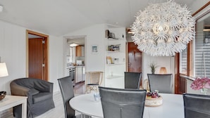 A modern living room with a dining area, featuring a white dining table, black chairs, a unique white chandelier, and a kitchen in the background. - "Herly" - 50m from the sea by Interhome (Hals)
