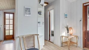 A hallway with a wooden floor, a wicker chair, a small table with a lamp, and a door with a frosted glass panel. - "Herly" - 50m from the sea by Interhome (Hals)