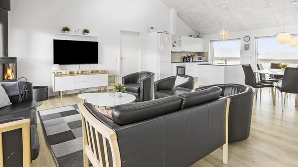 A modern living room with a fireplace, a flat-screen TV, a sofa, and a dining area with chairs and a table.
