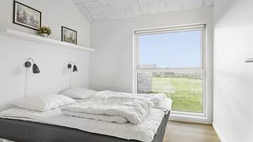 Une chambre moderne avec une grande fenêtre, un lit recouvert de linge de lit blanc et deux lampes fixées au mur.