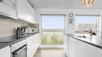 Une cuisine moderne avec des meubles blancs, un four encastré, un four à micro-ondes et une grande fenêtre donnant sur l’extérieur.