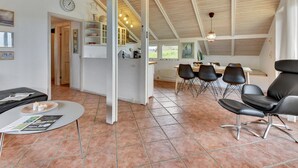 Una habitación amplia con techo alto, un comedor con sillas y mesa, y una cocina con armarios y un reloj.
