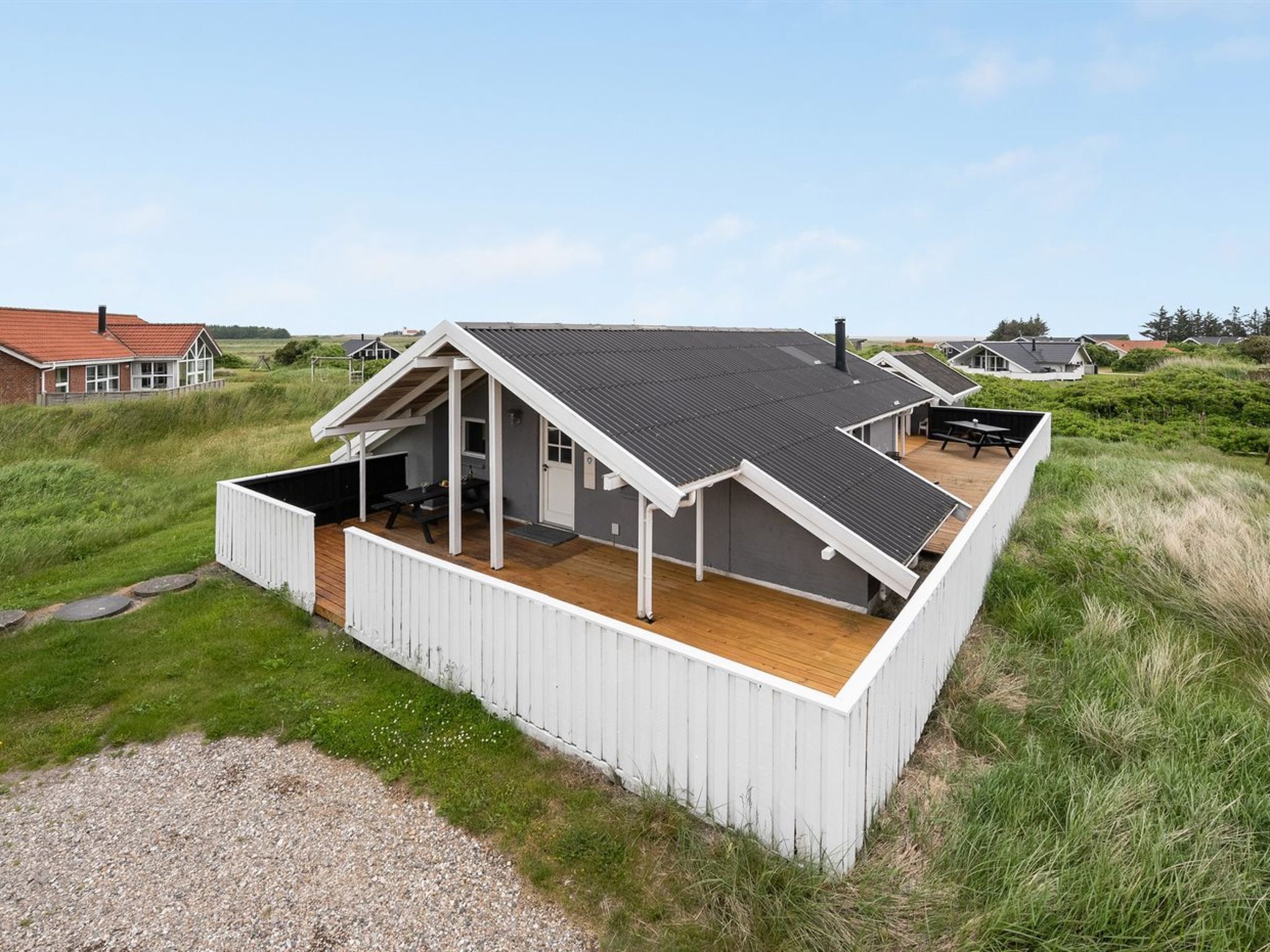 Ein modernes Haus mit einem geneigten Dach, einer Holzterrasse und einer überdachten Veranda.
