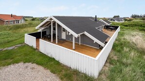 Una casa moderna con techo inclinado, terraza de madera y zona de patio techada.
