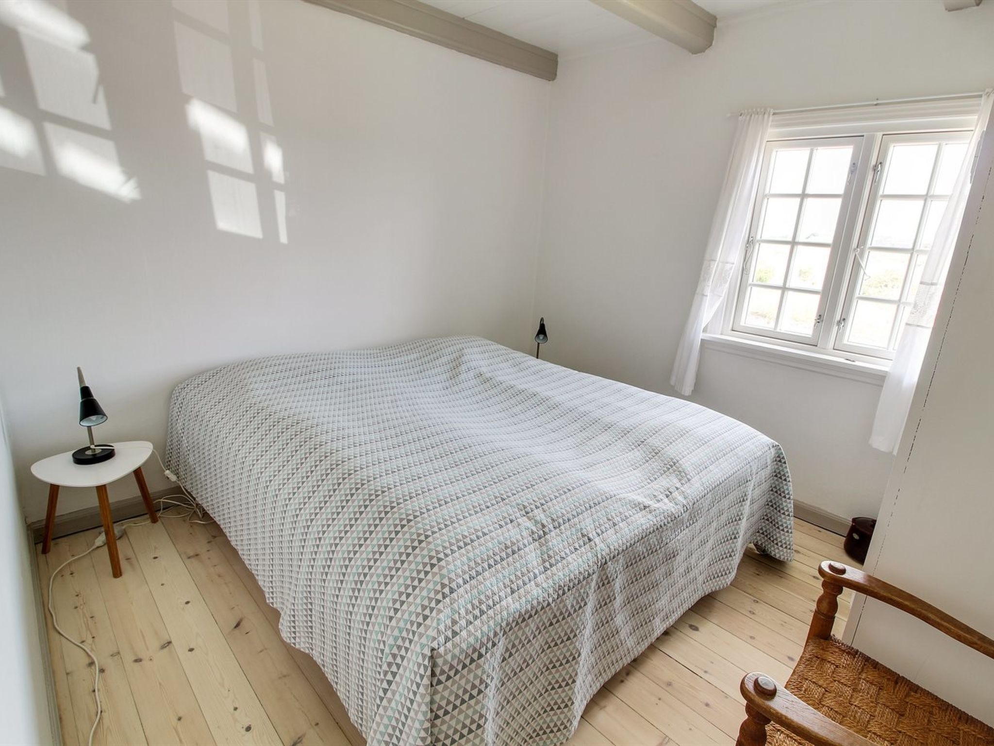 Une chambre à coucher avec un lit, une petite table, une lampe, une fenêtre et une chaise.