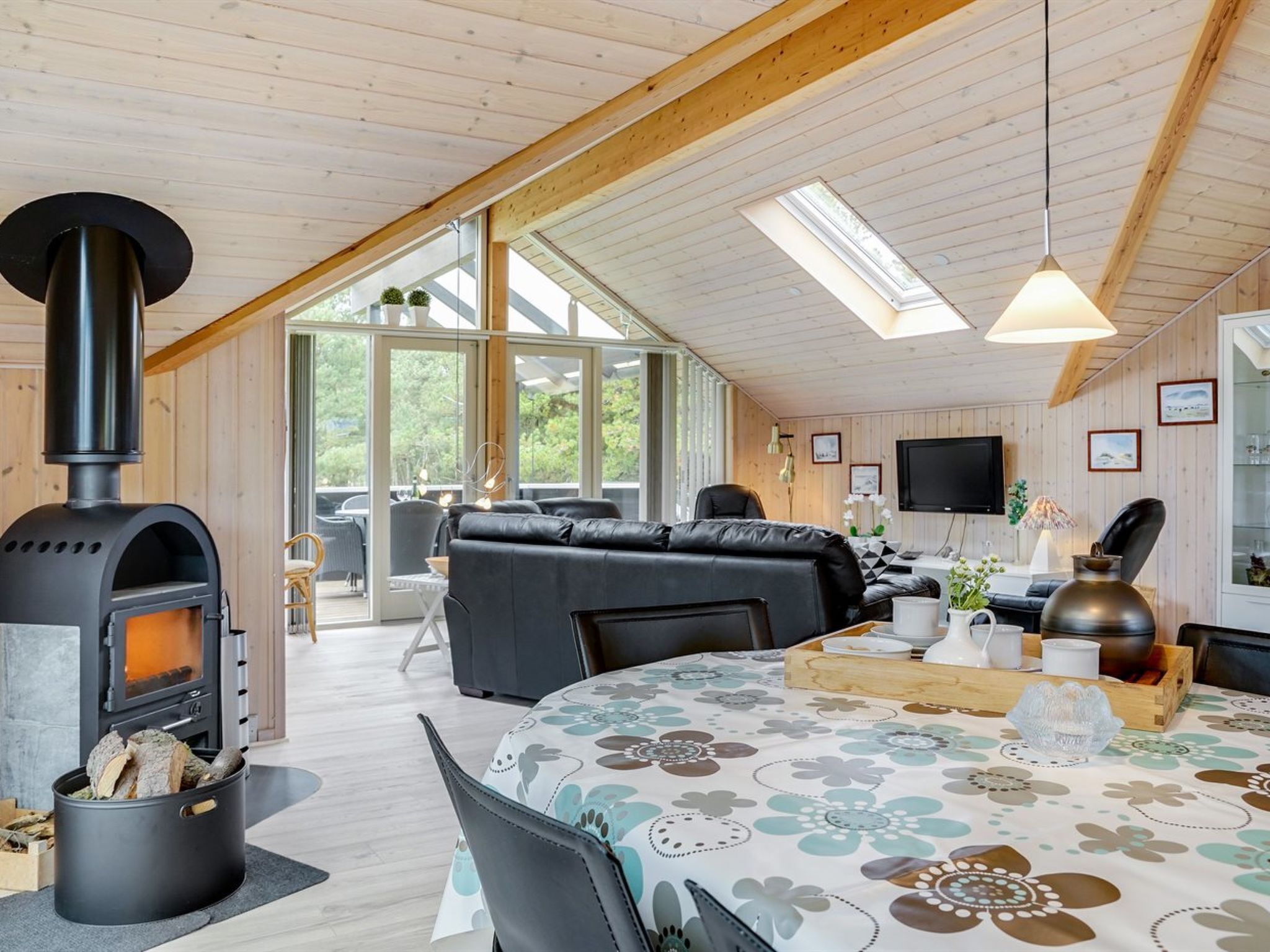 A cozy cabin interior with a wood-burning stove, a sofa, a dining table, and a TV.