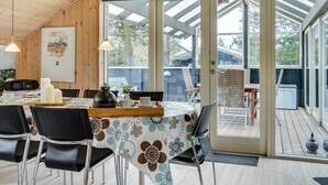 Comedor con techo de madera, un reloj y vistas al exterior a través de puertas de vidrio.
