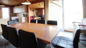 Ett rymligt matområde med ett träbord och svarta stolar, ett kök med vita skåp och utsikt över omgivningen genom stora fönster.