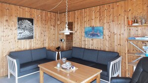 Ett mysigt rum med ett träpanelat tak, en mörkblå soffa, ett träbord med glas och en bokhylla.