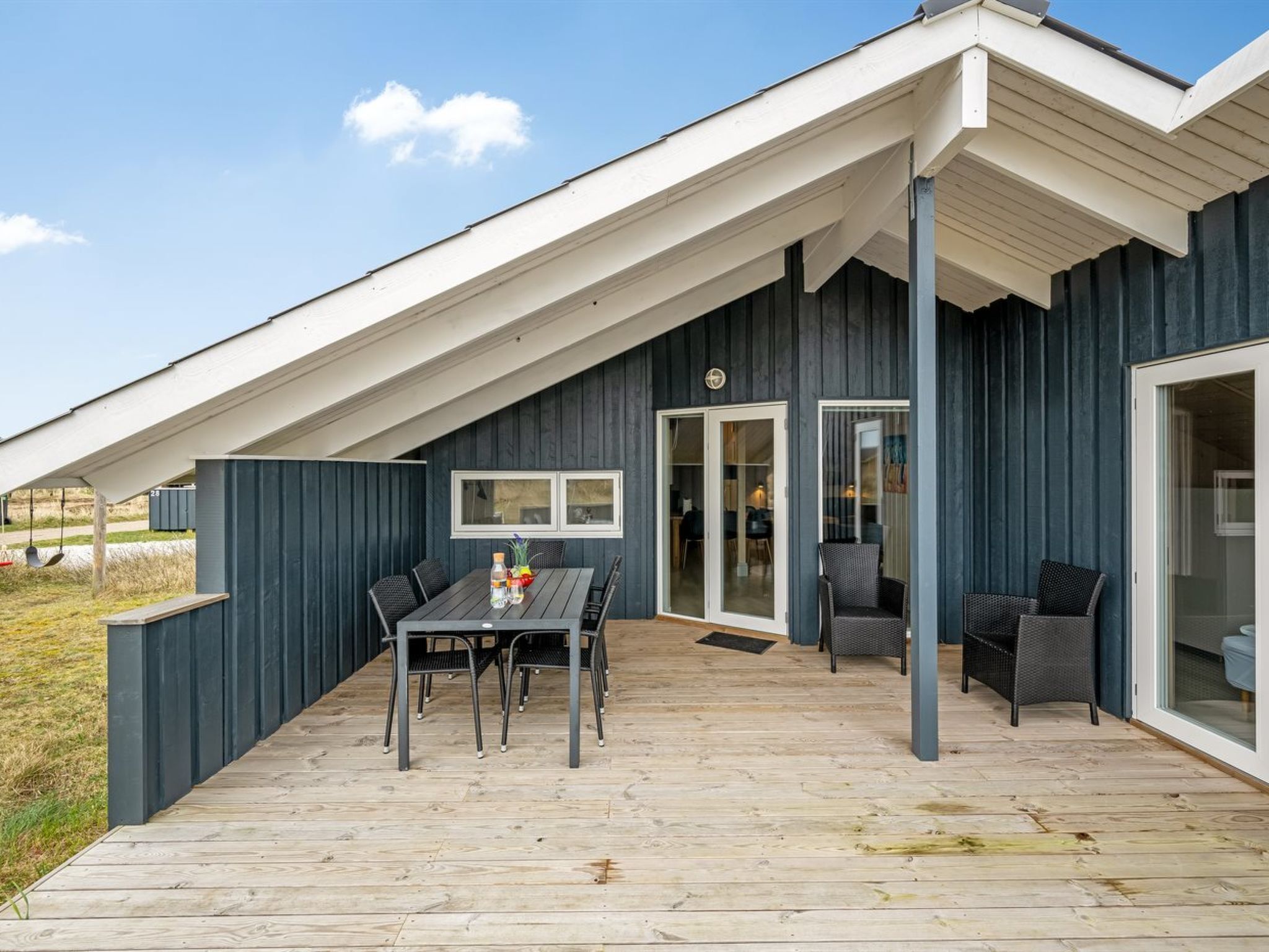 A modern house with a wooden deck, a dining area with a table and chairs, and a covered patio with seating.