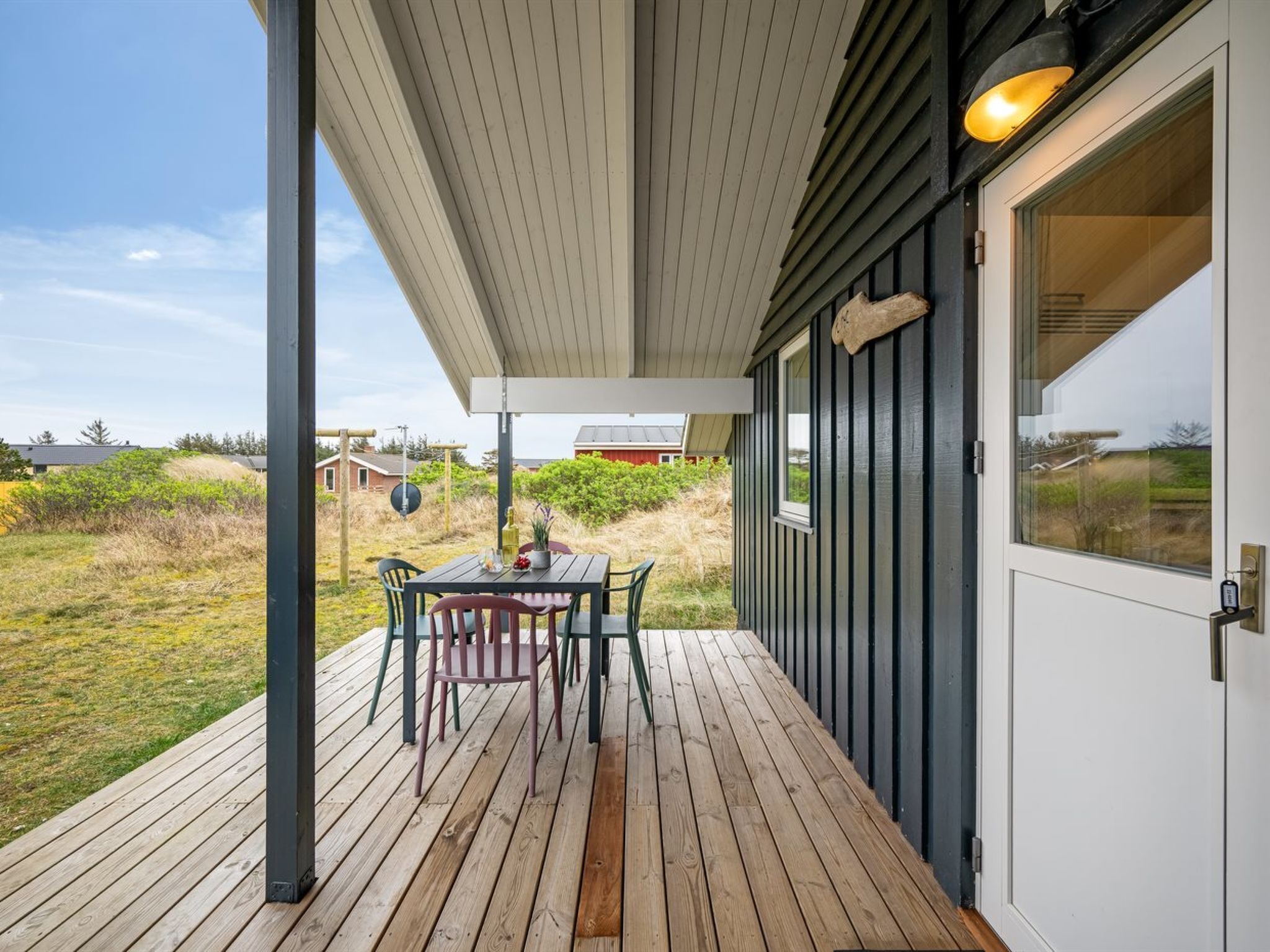 Een overdekt buitengebied met een tafel en stoelen, een houten terras en uitzicht op het omliggende landschap.