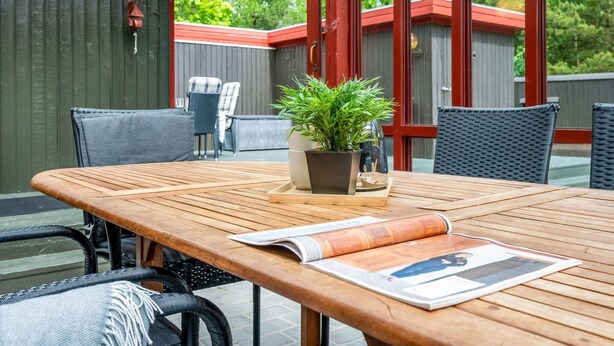 Eine Terrasse im Freien mit einem Holztisch, Stühlen, einem Blumentopf und einer Zeitschrift.