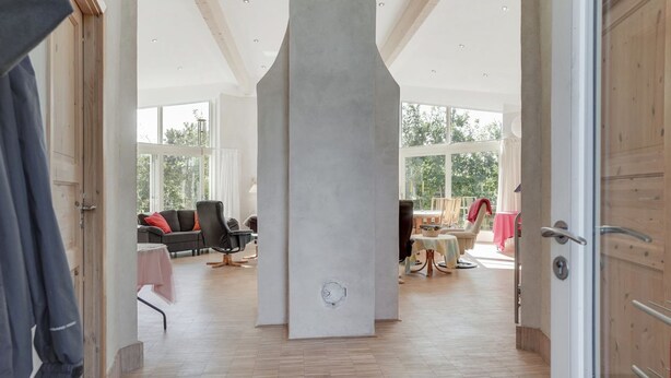 Een ruim interieur met een hoge plafond, een centrale kolom en uitzicht op een eetgedeelte met een tafel en stoelen.