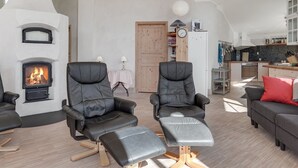 Een moderne woonkamer met twee leren fauteuils, een open haard, een keukenhoek en een houten deur.