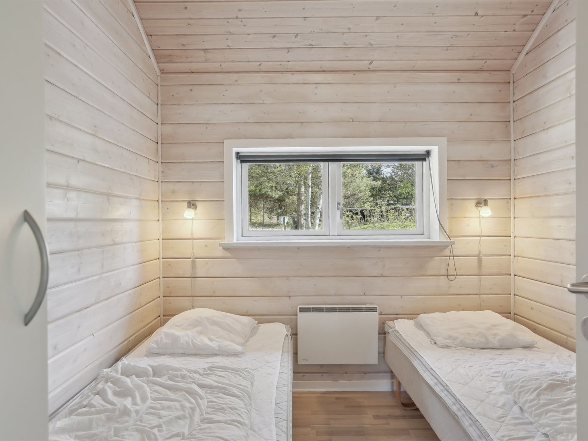 Uma cabana pequena, com um quarto, duas camas, uma janela e um radiador.