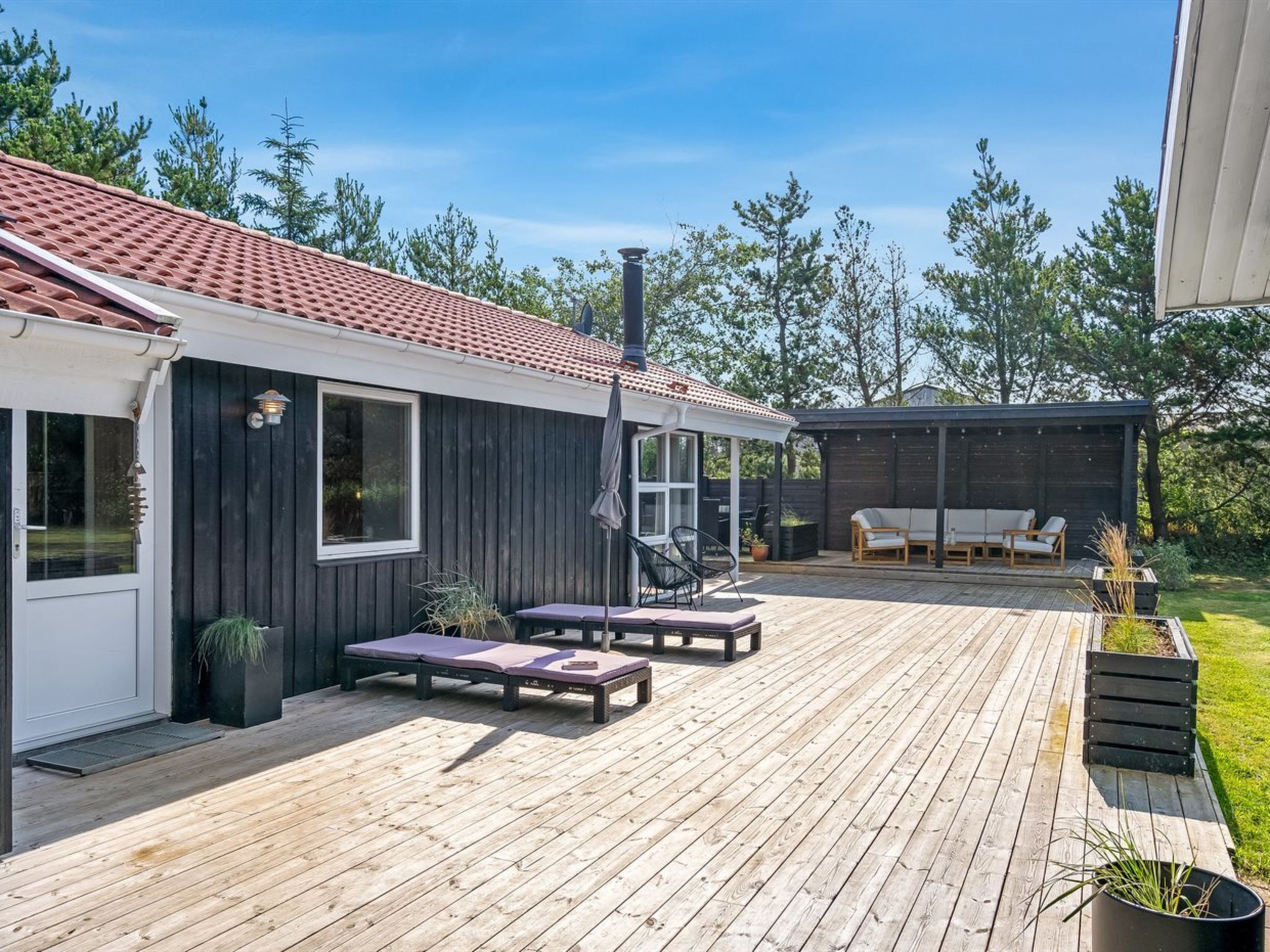 Une terrasse en bois avec deux chaises longues et un espace barbecue.
