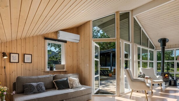 Een moderne woonkamer met een grijze bank, een witte fauteuil en een glazen deur naar een buitenruimte.