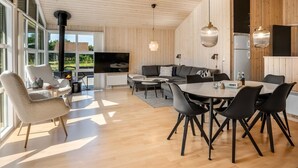 Een moderne woonkamer met een grote televisie, houten plafond en een eethoek met zwarte stoelen en een ronde tafel.
