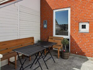 A patio with a wooden bench and table, a potted plant, and a brick wall with a window.