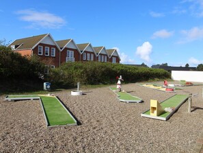 A miniature golf course with a gravel surface, green putting areas, and a red and white golf hole.