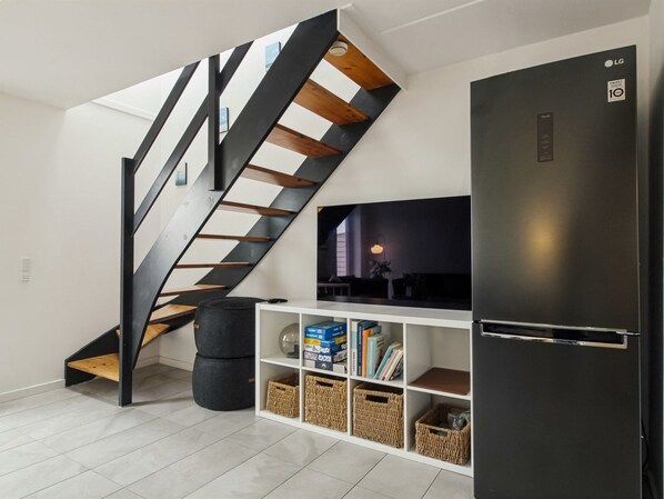 A modern living space with a black staircase, a flat-screen TV, and a black refrigerator.