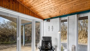 A modern room with a leather chair, a small table with a bottle and glasses, and a view of the outdoors through large sliding doors. - "Askatla" - 800m from the sea by Interhome (Ringkøbing)