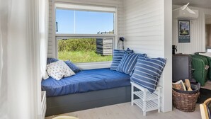 Ein Zimmer mit Fenster, einem Bett mit blauer Bettwäsche, einem kleinen weißen Stuhl, einem Korbwesen und einer Heizung.