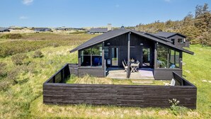 Eine moderne Holzblaus mit großem Panoramafenster, einer Terrasse und Blick auf die umliegende Landschaft.