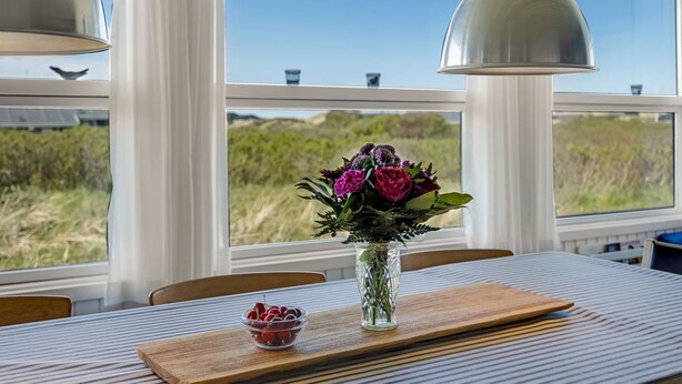 Ein Essbereich mit Tisch, Stühlen, einer Vase mit Blumen und einer Schale voll Kirschen.