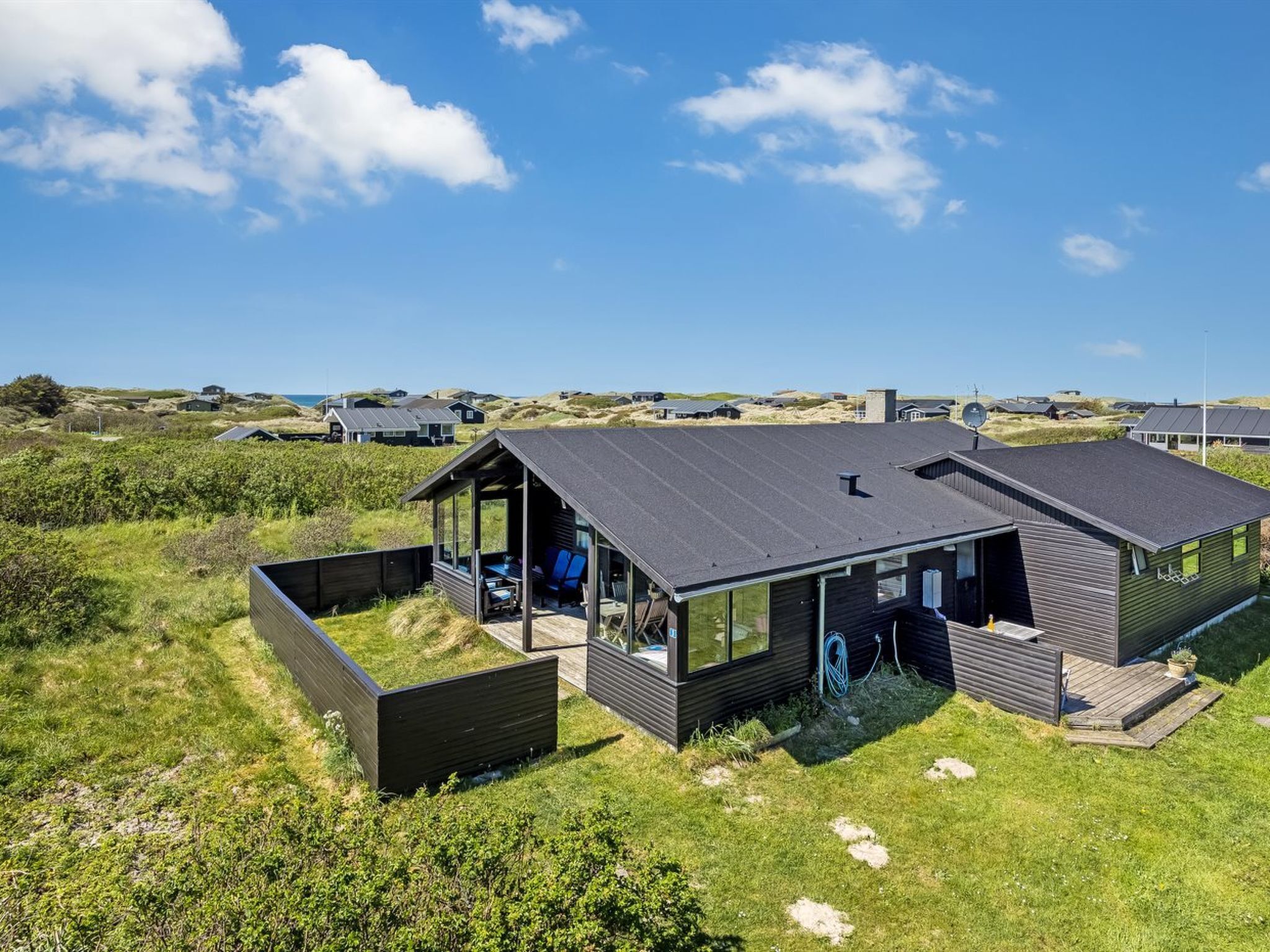 Une maison moderne dotée d’un porche vitré, d’une terrasse et offrant une vue sur le paysage environnant.