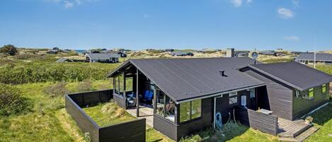 Une maison moderne dotée d’un porche vitré, d’une terrasse et offrant une vue sur le paysage environnant.