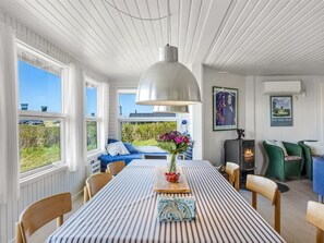 Un coin repas avec une nappe à rayures, un grand luminaire suspendu et une vue sur l’extérieur.
