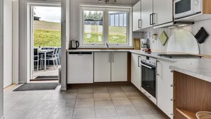 A modern kitchen with white cabinets, a built-in oven, microwave, and a large window offering a view of the outdoors.