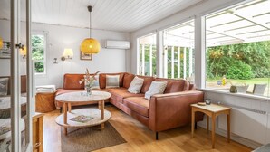 A modern living room with a brown leather sofa, a round wooden coffee table, and a view of greenery through large windows. - "Gia" - 1.3km from the sea by Interhome (Hals)