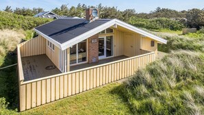 Ein modernes Strandhaus mit geneigtem Dach, großen Glasfenstern und einer Holterrasse.
