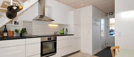 A modern kitchen with white cabinetry, a built-in oven, and a wooden staircase.