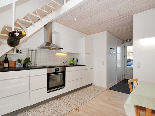 A modern kitchen with white cabinetry, a built-in oven, and a wooden staircase.