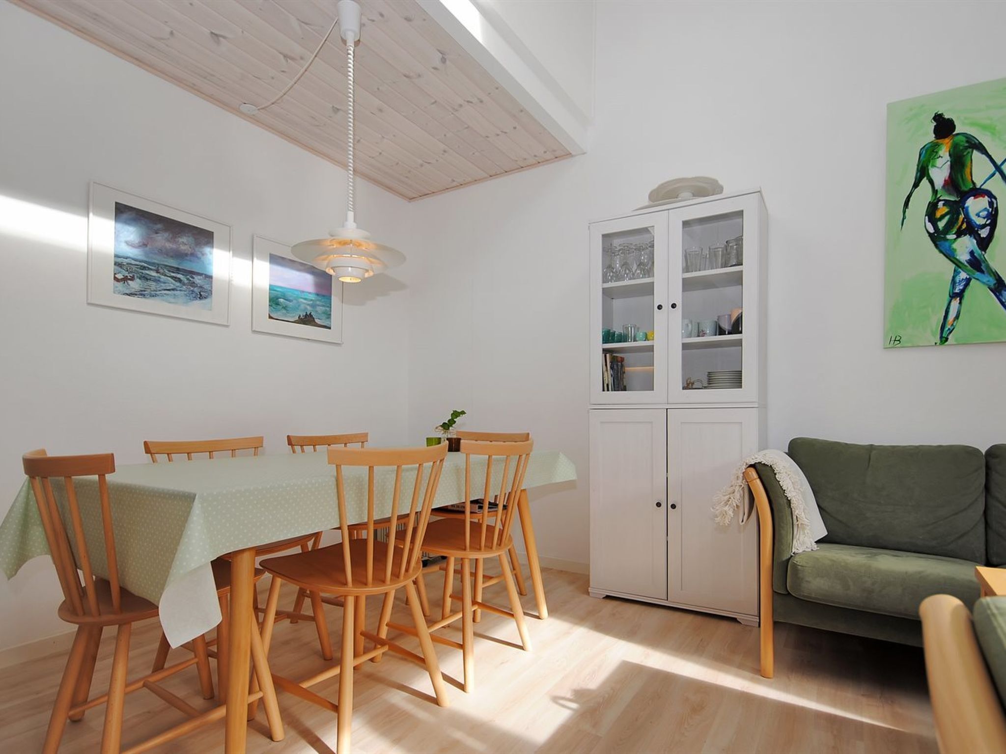 A dining area with a wooden table and chairs, a cabinet with glass doors, and a green sofa.