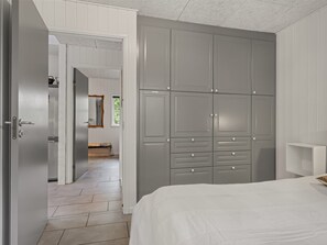 A bedroom with a large grey wardrobe, a bed, and a hallway leading to a bathroom.