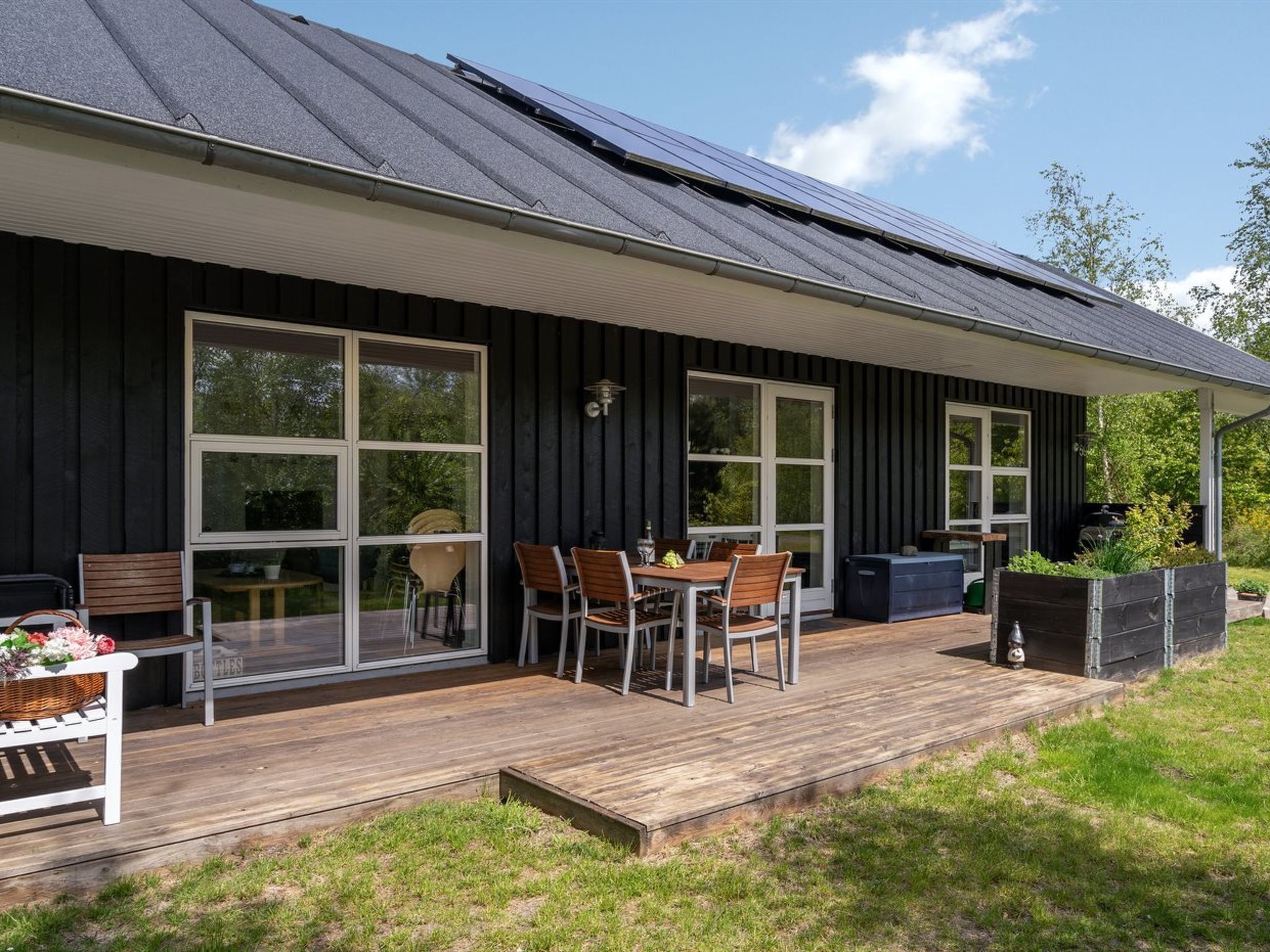 Une maison moderne dotée d’une terrasse, de grandes fenêtres et de panneaux solaires sur le toit.