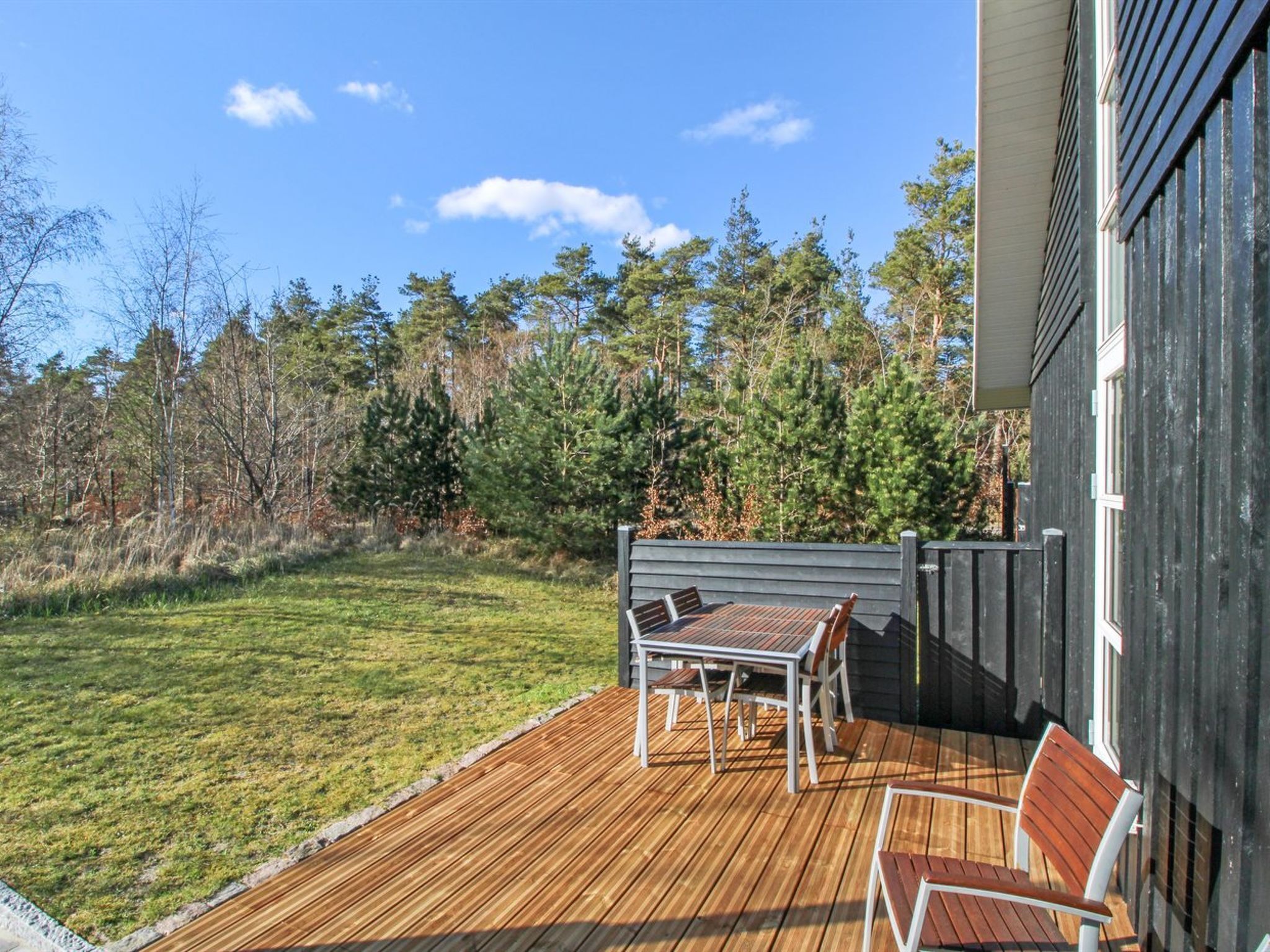 Une terrasse en bois avec une table et des chaises, entourée d’une pelouse et d’arbres.