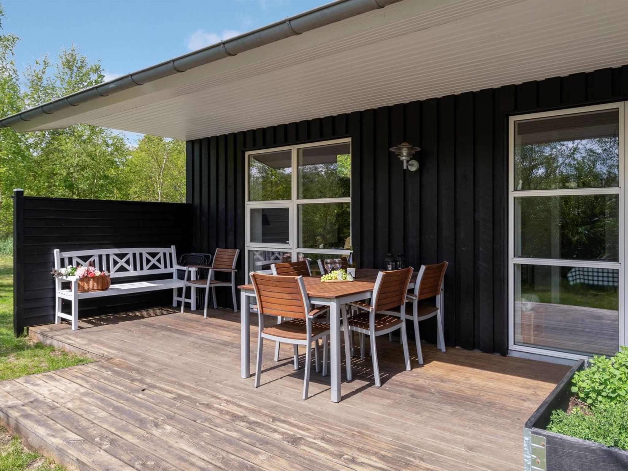 A wooden deck with a table and chairs, a bench, and a large window.