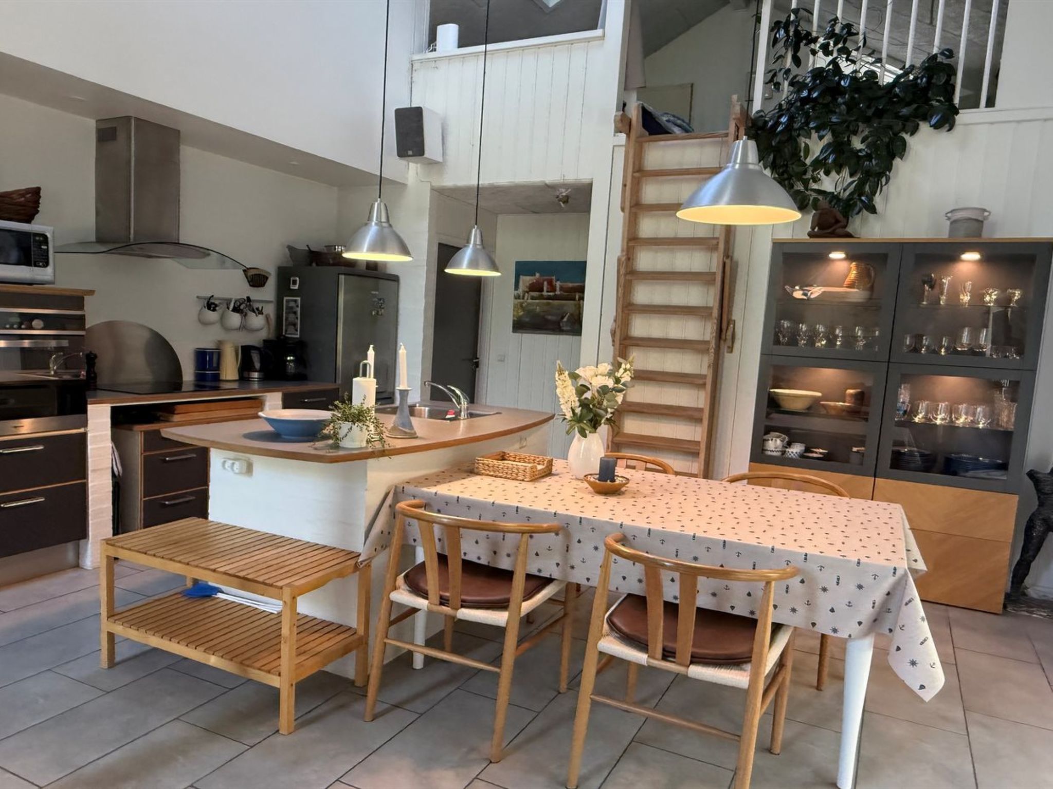 A compact kitchen with a central island, wooden chairs, and a dining table with a patterned tablecloth.