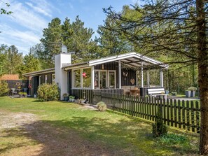 Une maison moderne de plain-pied, dotée d’un porche abrité, d’une cour clôturée et d’un drapeau sur la porte.