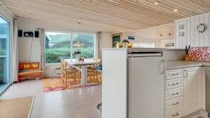 A modern kitchen with white cabinets, a dining area with a table and chairs, and a view of greenery outside.