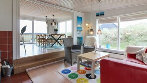 A spacious living area with a red sofa, a dining table with chairs, and a colorful rug.