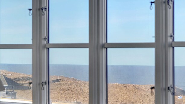 Blick durch ein mehrteiliges Fenster auf eine karge Landschaft mit weiter Wasserfläche.