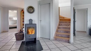 Ein Zimmer mit Kaminofen, einer Treppe und einer Tür zu einem weiteren Raum.