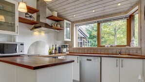 A modern kitchen with a built-in microwave, coffee maker, and dishwasher. There is a window providing natural light and a view of trees outside.