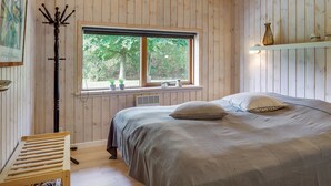 A wooden-paneled bedroom with a bed, a window, a radiator, and a shelf with decorative items.
